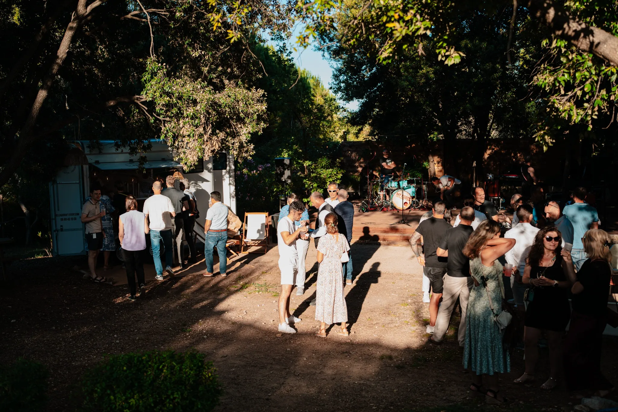 Ambiance d’événement professionnel en extérieur : invités réunis sous les arbres devant une scène de concert